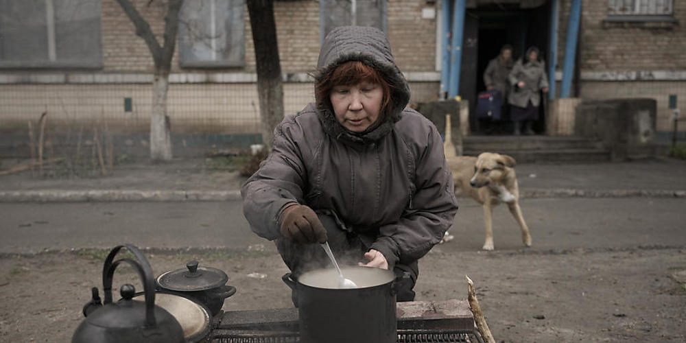 Eine Frau kocht auf einem offenen Feuer vor einem Wohnhaus in Butscha. Foto: Vadim Ghirda/AP/dpa
