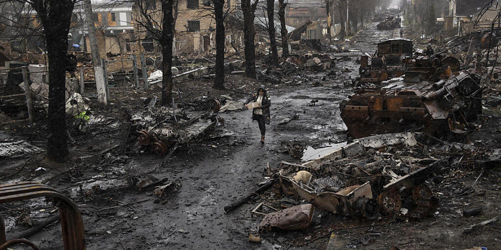 dpatopbilder - Eine Frau auf einer mit zerstörten russischen Militärfahrzeugen übersäten Straße in Butscha. Foto: Rodrigo Abd/AP/dpa