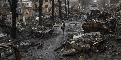 dpatopbilder - Eine Frau auf einer mit zerstörten russischen Militärfahrzeugen übersäten Straße in Butscha. Foto: Rodrigo Abd/AP/dpa