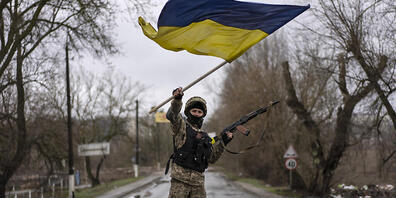 Ein ukrainischer Soldat steht an einer Straßenblockade in Butscha und hält die ukrainische Flagge hoch. Foto: Rodrigo Abd/AP/dpa