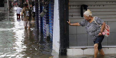 ARCHIV - Eine ältere Frau versucht sich den Weg über eine überschwemmte Straße zu bahnen. Nach den Erdrutschen und Überschwemmungen in Folge von heftigem Regen in Brasilien ist die Zahl der Toten auf mindestens 20 gestiegen, teilte das Nachrichten...