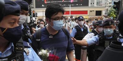 Polizisten stoppen und durchsuchen einen Mann, der einen Blumenstrauß in der Nähe des Victoria Parks in Hongkong hält. Foto: Kin Cheung/AP/dpa