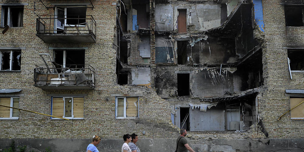 Menschen tragen humanitäre Hilfsgüter an einem zerstörten Wohnhaus vorbei, das durch den Beschuss der russischen Armee beschädigt wurde. Foto: Sergei Chuzavkov/SOPA Images via ZUMA Press Wire/dpa
