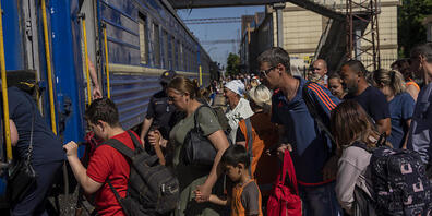 Personen besteigen einen Evakuierungszug auf einem Gleis. Foto: Bernat Armangue/AP/dpa
