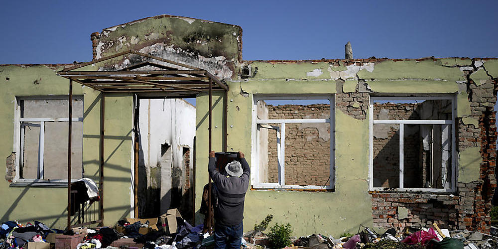 Ein Mann sucht nach Kleidung vor einem durch Angriffe zerstörten Gebäude. Foto: Natacha Pisarenko/AP/dpa