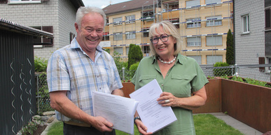 Gemeinderat Josef Bruhin hat die Petition mitunterzeichnet, Ursula Bruhin, eine der Initiantinnen, hält die Einsprache gegen die geplante zweite 5G-Antenne in der Hand. Im Hintergrund sind die Bauprofile auf dem Dach des Mietshauses zu sehen. 