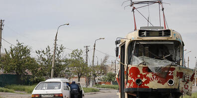 Ein Mann schiebt ein liegengebliebenes Auto an einer beschädigten Straßenbahn in Mariupol vorbei. Foto: Alexei Alexandrov/AP/dpa