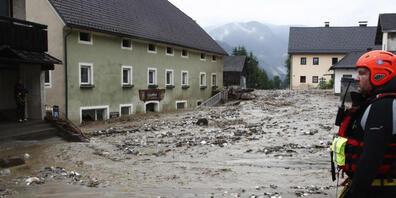 Eine Einsatzkraft sieht sich die Schäden nach einem Unwetter an. Schwere Unwetter haben ganze Ortschaften im Bezirk Villach-Land verwüstet. Foto: Gert Eggenberger/APA/dpa