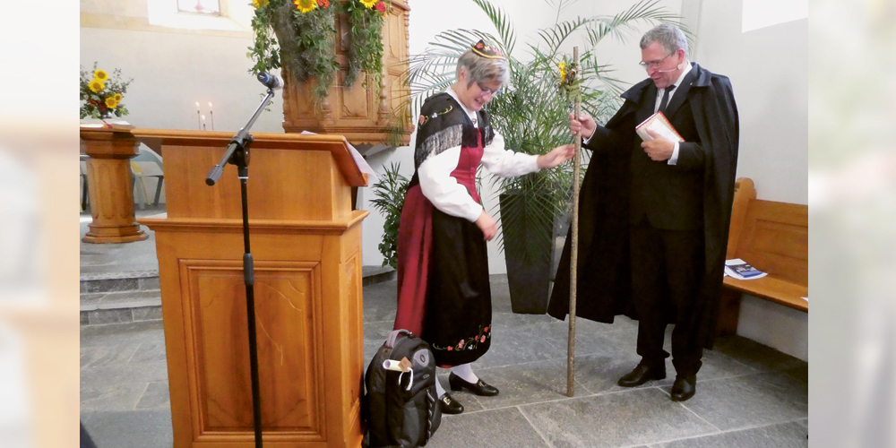 Pfarrer Jan-Andrea Bernhard erhielt von Elsbeth Gabathuler,  Präsidentin der Kirchenregion Herrschaft – Fünf Dörfer,  einen Wanderstab mit Rucksack. 
