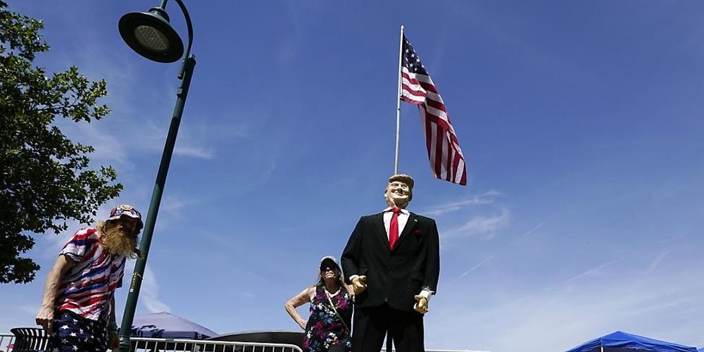 Anhänger des ehemaligen US-Präsidenten Trump halten vor einer Trump-Statue inne, Stunden vor Trumps Rede bei einer "Save America"-Kundgebung. Foto: Ross D. Franklin/AP/dpa