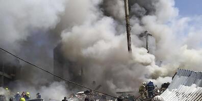 Zivilisten und Feuerwehrleute befinden sich an der Unfallstelle während Rauch aufsteigt. Nach einer schweren Explosion in einem Einkaufszentrum sind nach offiziellen Angaben einige Menschen verletzt oder tot. Foto: Daniel Bolshakov/AP/dpa