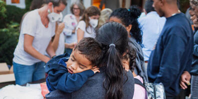 ARCHIV - Eine Frau, die zu einer Gruppe gerade angekommener Einwanderer gehört, hält ein Kind vor der St. Andrews-Kirche auf Martha's Vineyard. Foto: Ray Ewing/Vineyard Gazette/dpa