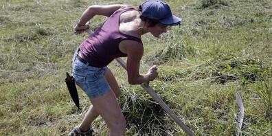 Eine Bäuerin schneidet mit ihrer Sense Gras an einem Bachbord im Schwyzerischen Schübelbach. (Archivbild)