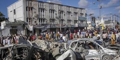 dpatopbilder - Menschen gehen an zerstörten Autos und Häusern vorbei, wo am Vortag zwei Autobomben an einer belebten Kreuzung in Mogadischu in Somalia eingeschlagen sind. Foto: Farah Abdi Warsameh/AP/dpa