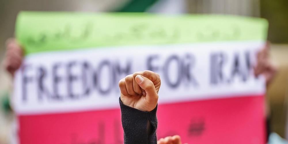 Eine Faust reckt sich vor einem Plakat mit der Aufschrift "Freedom for Iran", während Demonstranten bei einer Kundgebung vor der Alten Oper stehen, um gegen die gewaltsame Niederschlagung regimekritischer Demonstrationen im Iran nach dem Tod von M...