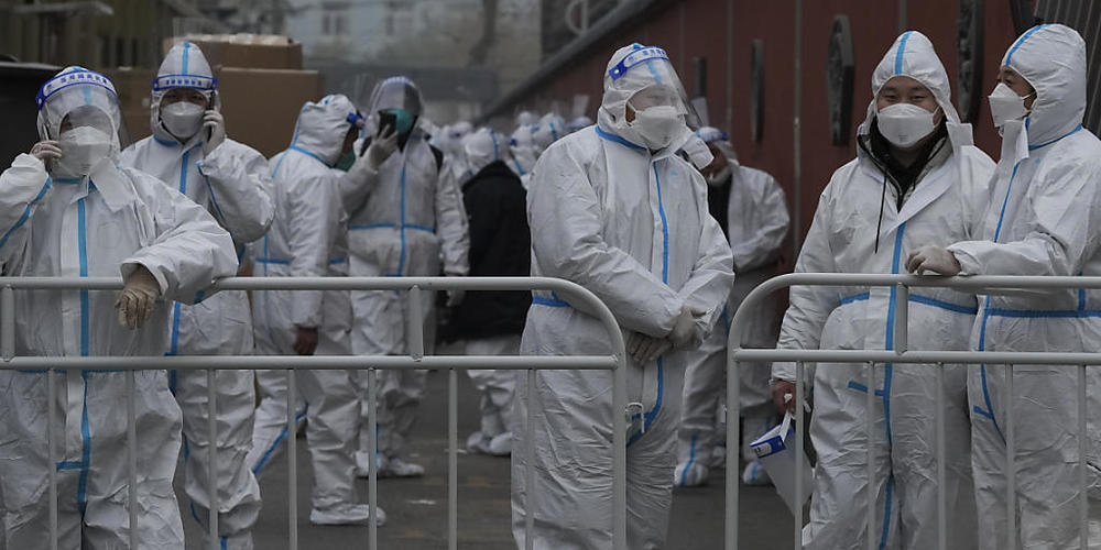 Arbeiter in Schutzanzügen in einem abgesperrten Viertel. Foto: Andy Wong/AP/dpa