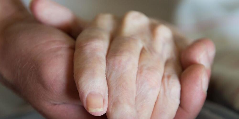 Ein Altenpfleger hält in einem Pflegeheim die Hand einer Frau. (Symbolbild)