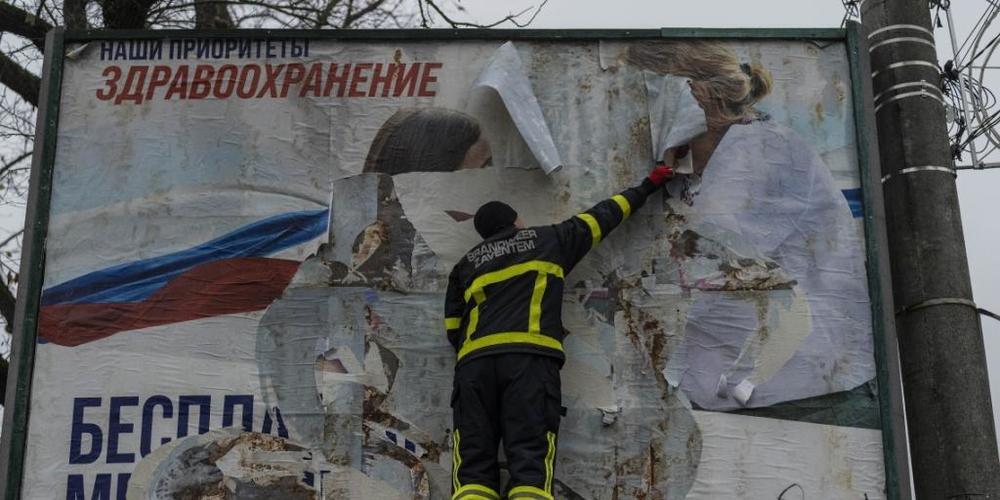 Ein ukrainischer Feuerwehrmann reißt in der kürzlich befreiten Stadt Cherson eine russisches Werbeplakat von einer Werbetafel. Foto: Bernat Armangue/AP/dpa