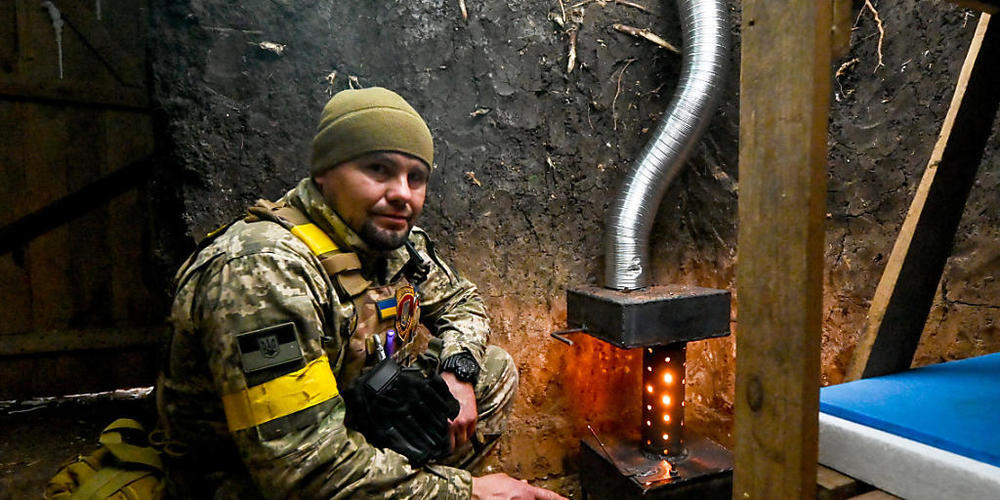 Ein ukrainischer Soldat wärmt sich an einem Ofen. Foto: ---/Ukrinform/dpa