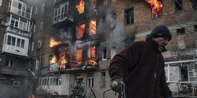 dpatopbilder - Ein Anwohner verlässt sein Wohnhaus in Bachmut, das nach einem Beschuss in Flammen steht. Foto: Libkos/AP/dpa