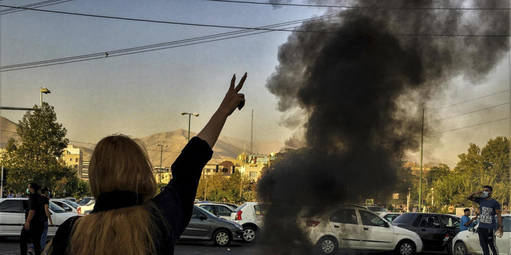 ARCHIV - Eine Frau steht während einer Demonstration nach dem Tod der 22-jährigen Mahsa Amini vor einem brennenden Autoreifen und zeigt das Victory-Zeichen. Foto: Uncredited/AP/dpa