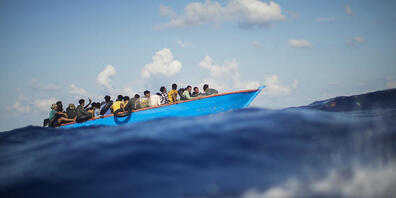 ARCHIV - Migranten sitzen in einem Holzboot südlich der italienischen Insel Lampedusa auf dem Mittelmeer. Foto: Francisco Seco/AP/dpa