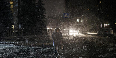 Eine Frau überquert bei Schneefall die Straße in Kiew - die Stromversorgung ist ausgefallen. Foto: Felipe Dana/AP/dpa