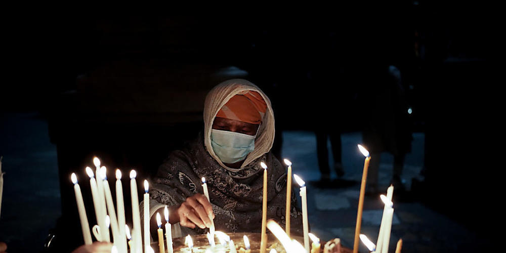 ARCHIV - Eine Frau mit Mund-Nasen-Schutz zündet Kerzen an und betet an Heiligabend in der Grabeskirche in Jerusalem. Foto: Nir Alon/ZUMA Press Wire/dpa