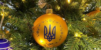 An einem geschmückten Baum in einem Geschäft hängt eine Kugel in den ukrainischen Nationalfarben Blau und Gelb mit dem Dreizack als Wappen. Foto: Ulf Mauder/dpa