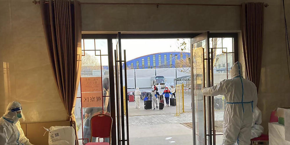 Arbeiter in Schutzkleidung bereiten die Aufnahme von Passagieren vor, die in ein Resort am Stadtrand von Peking in Quarantäne gebracht werden sollen. Foto: Ken Moritsugu/AP/dpa
