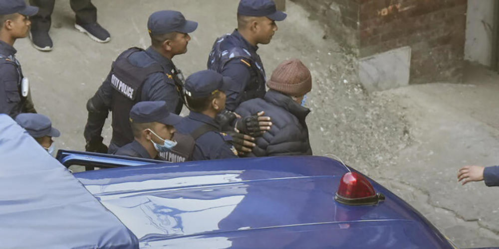 Nepalesische Polizisten eskortieren einen französischen Serienmörder (M, mit brauner Mütze) zur Migrationsbehörde in Kathmandu. Foto: Niranjan Shrestha/AP/dpa