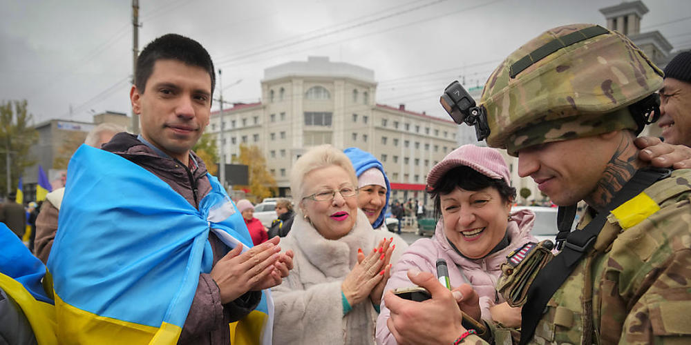 Einwohner von Cherson applaudieren den Soldaten, während ein ukrainischer Soldat seine Wünsche für einen in die Nationalflagge eingewickelten Mann schreibt. Foto: Efrem Lukatsky/AP/dpa