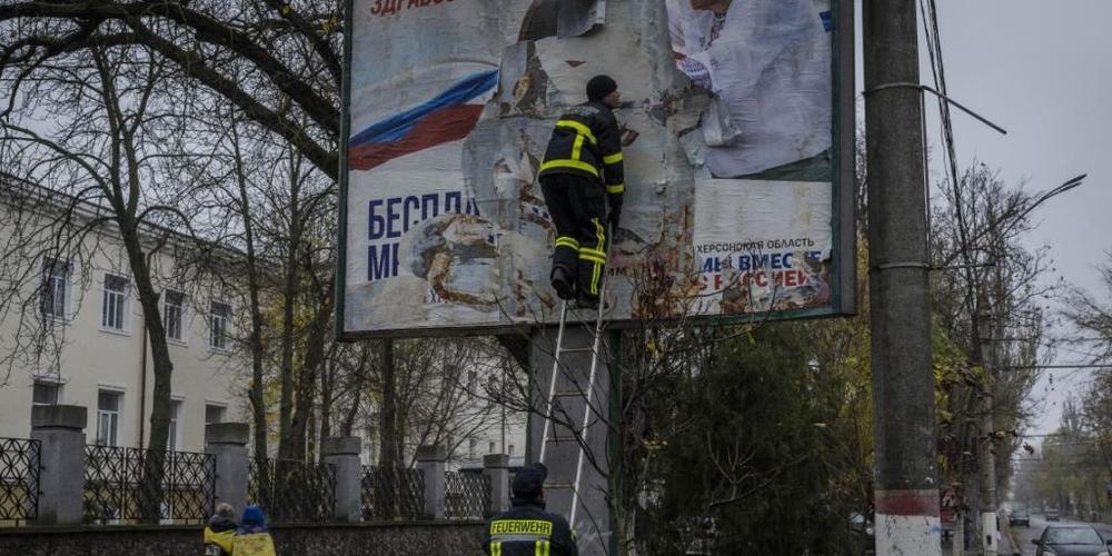 Feuerwehrleute entfernen russische Plakate in Cherson. Foto: Bernat Armangue/AP/dpa