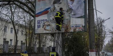 Feuerwehrleute entfernen russische Plakate in Cherson. Foto: Bernat Armangue/AP/dpa