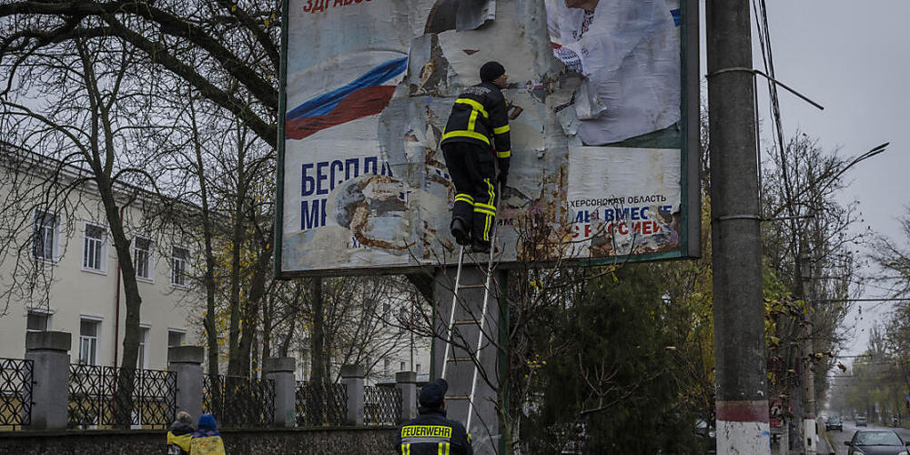 Nach der Rückeroberung von Cherson entfernen Feuerwehrleute russische Plakate. Nach Einschätzung des britischen Geheimdienst stellt Russland sich im Moment auf weitere Verluste ein. Foto: Bernat Armangue/AP/dpa