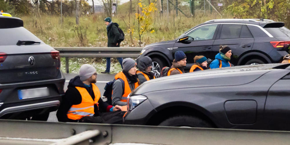 Teilnehmer eines Klimaprotests blockieren auf der A113 kurz vor der Ausfahrt zum Flughafen Berlin Brandenburg (BER) "Willy Brandt" den Verkehr. Foto: Christoph Soeder/dpa