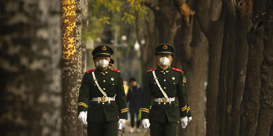 Chinesische paramilitärische Polizisten mit medizinischen Masken gehen eine Straße in Peking entlang. Foto: Mark Schiefelbein/AP/dpa