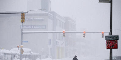 Eine Person überquert die Ellicott Street bei Schneefall. Ein gefährlicher Schneesturm hat Teile des westlichen und nördlichen New Yorks lahmgelegt, wobei mancherorts bisher schon fast 60 cm Schnee liegt. Foto: Joshua Bessex/FR171816 AP/dpa