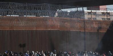 Migranten aus Lateinamerika stehen an der Grenzmauer zwischen Mexiko und den USA. Foto: Christian Chavez/AP/dpa