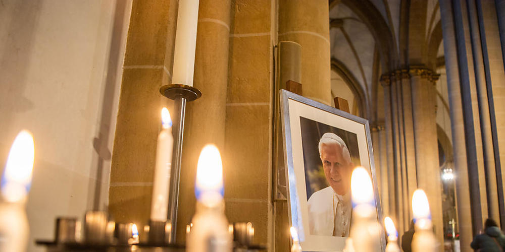 Ein Porträtbild vom emeritierten Papst Benedikt XVI. steht hinter Andachtskerzen im Paderborner Dom. Foto: Lino Mirgeler/dpa - ACHTUNG: Verwendung nur im vollen Format