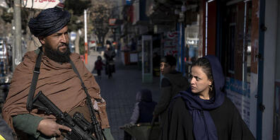 dpatopbilder - Ein Taliban-Kämpfer steht Wache, während eine Frau vorbeiläuft. Jüngste Entscheidungen der Taliban über afghanische Frauen, darunter das Verbot der Arbeit für Nichtregierungsorganisationen, lösten Proteste in den Großstädten aus. Fo...