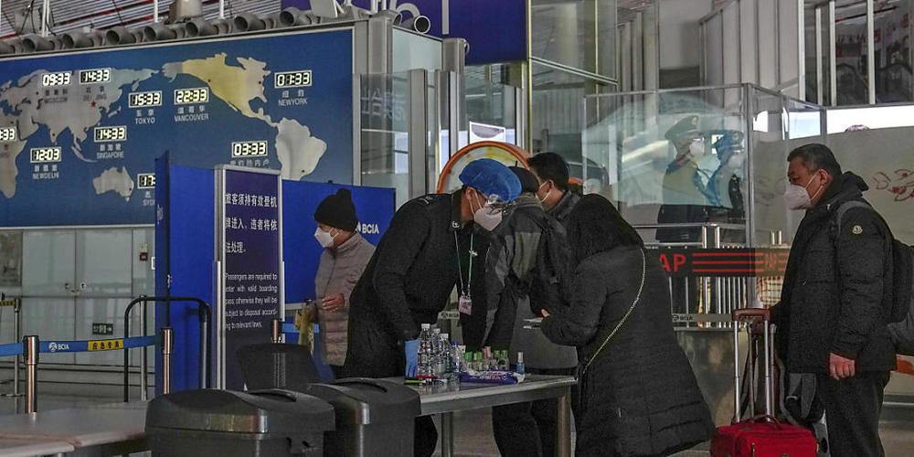 Passagiere mit Mund-Nasen-Schutz stellen sich an der Sicherheitskontrolle an, bevor sie zu einem internationalen Abfluggate am Flughafen Peking gehen. Foto: Andy Wong/AP/dpa