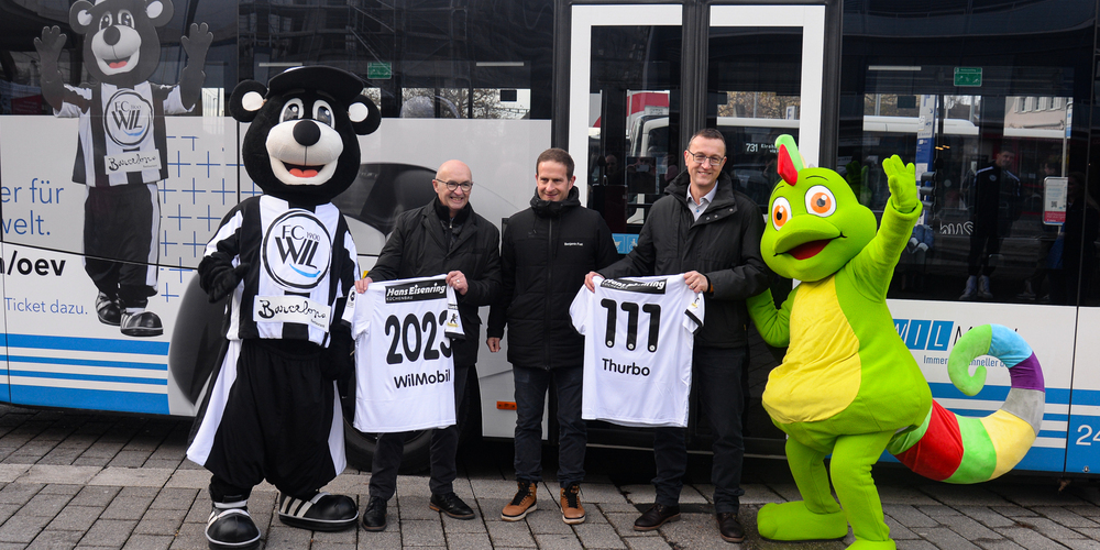 Hans Koller, Leiter Markt BUS Ostschweiz; Benjamin Fust, CEO FC Wil 1900 und Christian Baum- gartner, Leiter Markt Thurbo (von links) posieren mit den Maskottchen Willy und Thurbo vor dem Wil- Mobil-Bus mit brandneuer ÖV-Werbung. Spezialtrikots dürfen zur Feier der Partnerschaft nicht fehlen: 111 entspricht der Gesamtzahl an Zonen im OSTWIND-Gebiet. In diesen Zonen können Fussballfans mit gültigem Matchticket gratis per ÖV an die Heimspiele des FC Wil reisen.