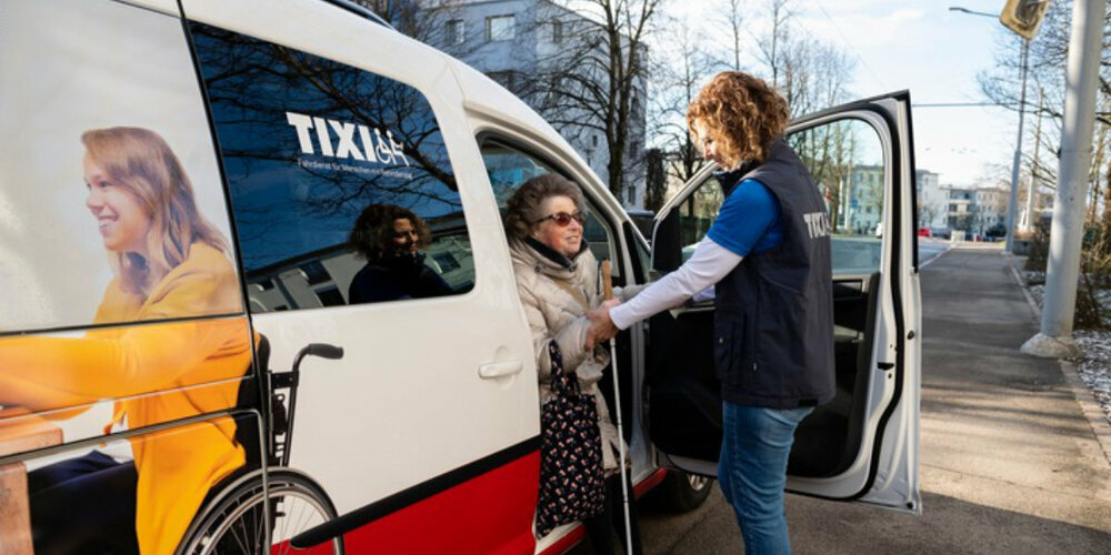 Eine freiwillige TIXI-Fahrerin hilft einem blindem Fahrgast beim Einsteigen ins TIXI.