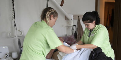Eine Lernende Fachfrau Gesundheit (rechts) kleidet zusammen mit einer Spitex-Mitarbeiterin einen körperlich stark eingeschränkten Mann an. Der Kanton Graubünden unterstützt in der Zukunft Betriebe bei der Ausbildung der Fachfrauen und Fachmän...