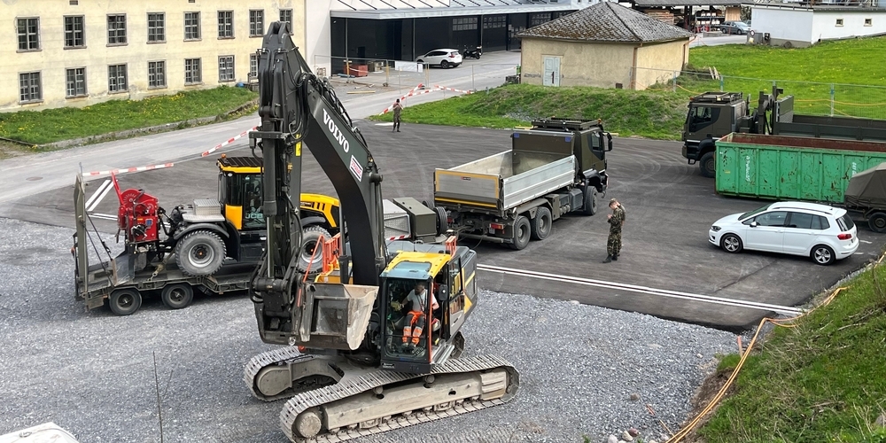 Vorne der erste angelieferte Bagger für die Räumung, hinten wird eine der Spezialmaschinen der Armee für den Abtransport verladen, nahe am befestigten Sortierplatz.