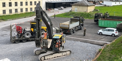 Vorne der erste angelieferte Bagger für die Räumung, hinten wird eine der Spezialmaschinen der Armee für den Abtransport verladen, nahe am befestigten Sortierplatz.