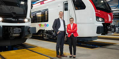 Werner Schurter (Verwaltungsratspräsident) und Claudia Bossert (Unternehmensleiterin) stehen im Werk von Stadler Rail zwischen der Gegenwart und der Zukunft von Thurbo: Links ist der aktuelle GTW zu sehen, rechts der künftige Flirt Evo.