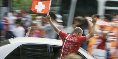 Ein feiernder Fussballfan lehnt sich während der Fahrt aus dem Auto und risikiert eine Anzeige. (Archivbild)