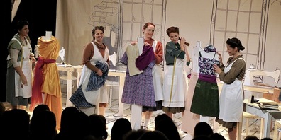 Die Schürzennäherinnen und ihre Vorarbeiterin versuchen sich in einer Pause an Entwürfen für die Modewelt